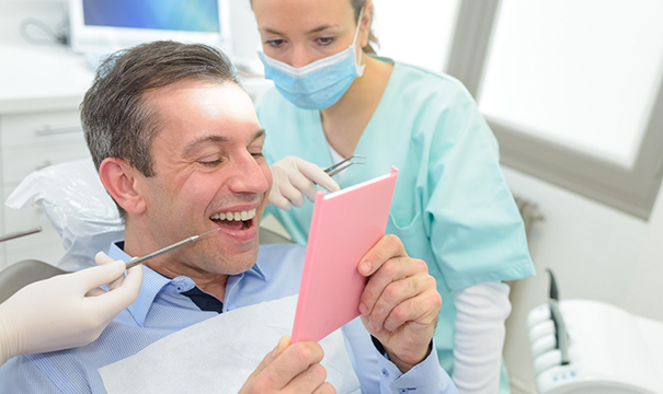 A male patient looking at his smile in the mirror after having dental crowns in Newton placed