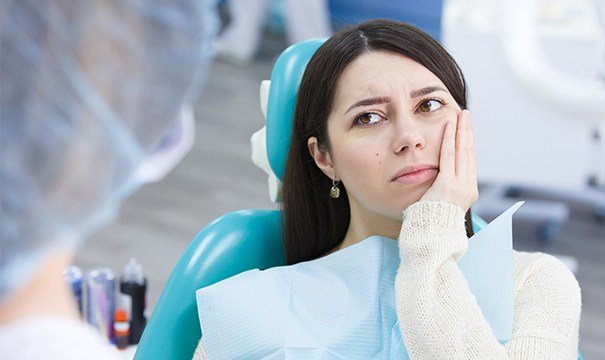 Woman in dental chair holding cheek in pain