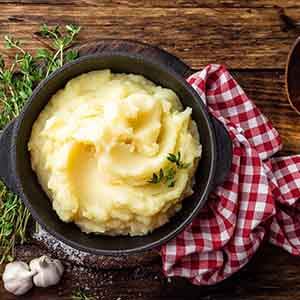Bowl of mashed potatoes on wooden table next to napkin and wooden spoon