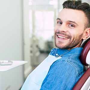 Man in denim jacket sitting in dental chair smiling