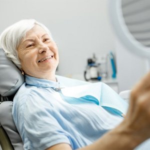 a patient checking her renewed smile with a mirror