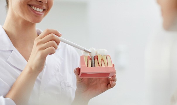Dentist showing patient model of dental implant in Newton, MA