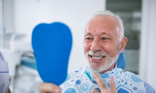 Senior male patient checking smile in a handheld mirror