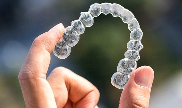 Close-up of hand holding aligner for Invisalign in Newton
