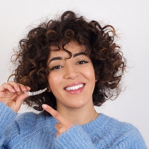 Woman in blue sweater holding up clear aligner