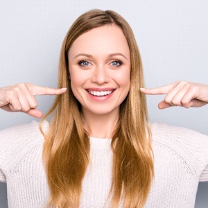 Woman pointing at her smile, happy she could afford Invisalign