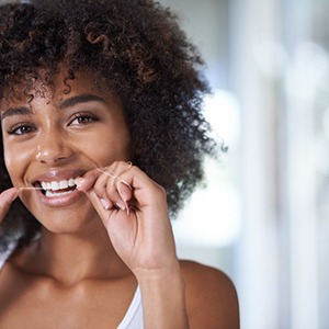 Woman with curly hair smiling while flossing her teeth