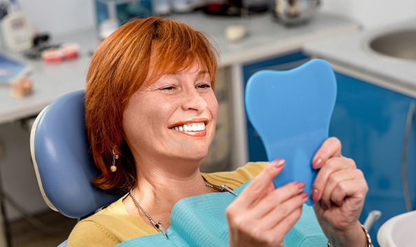 Woman at dentist office smiling into hand mirror 