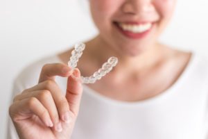 smiling person holding Invisalign tray 