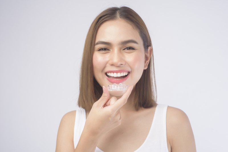 person smiling while holding Invisalign aligner