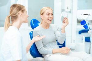 Patient in dentist's chair admiring smile in handheld mirror.