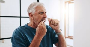 Man with white hair flossing teeth